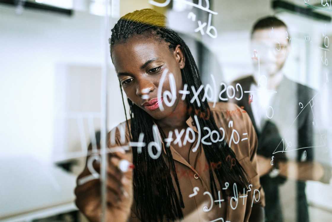 Colleagues writing mathematical formulas on transparent wipe board