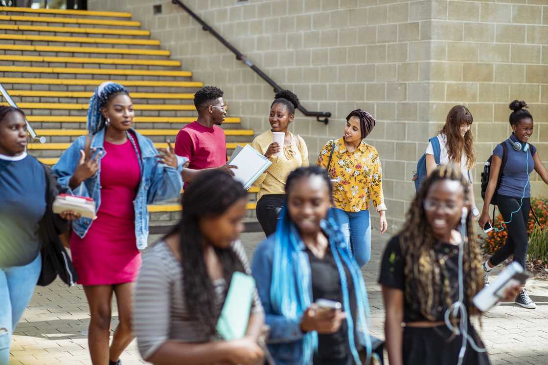 A diverse group of students in their 20's walking down some steps on campus laughing and talking to each other.