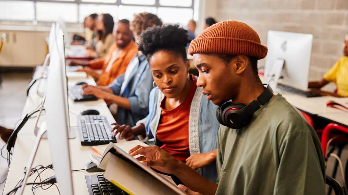 Male and female students read books in front of computers in a library.