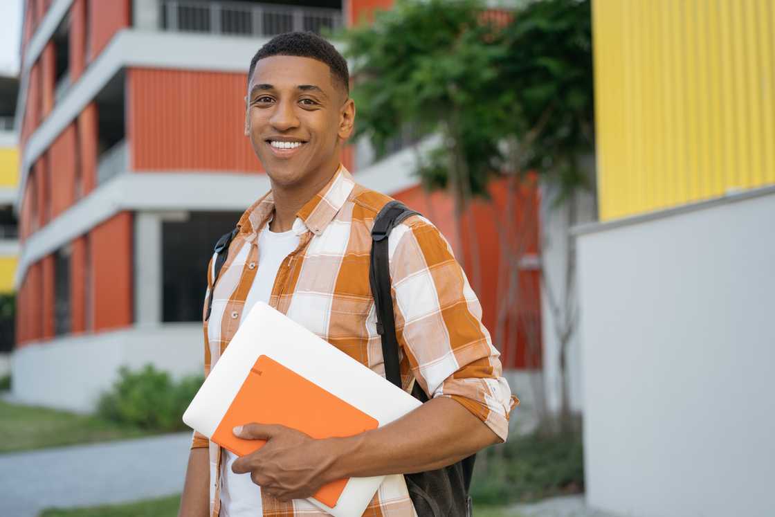 A male student walking in university campus holding books.