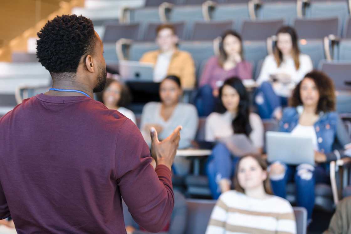 A college professor gestures while giving a lecture to a group of college students