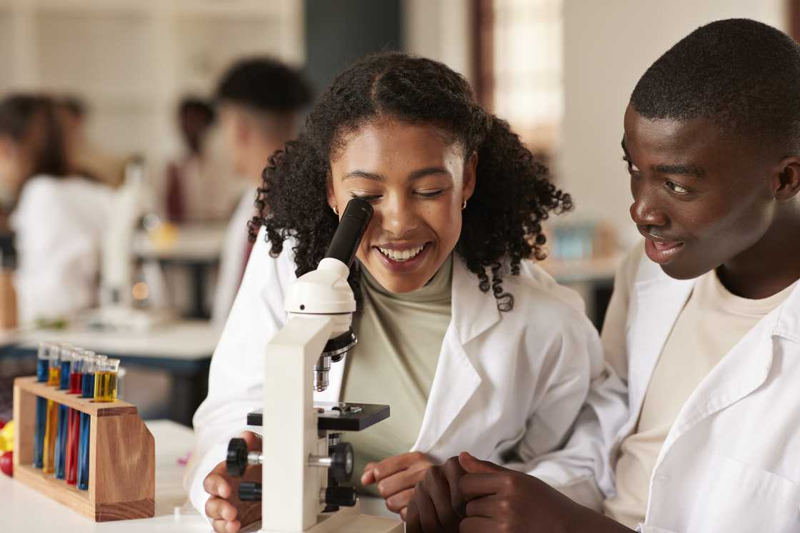 A female student looking through microscope with her friend sitting in science laboratory